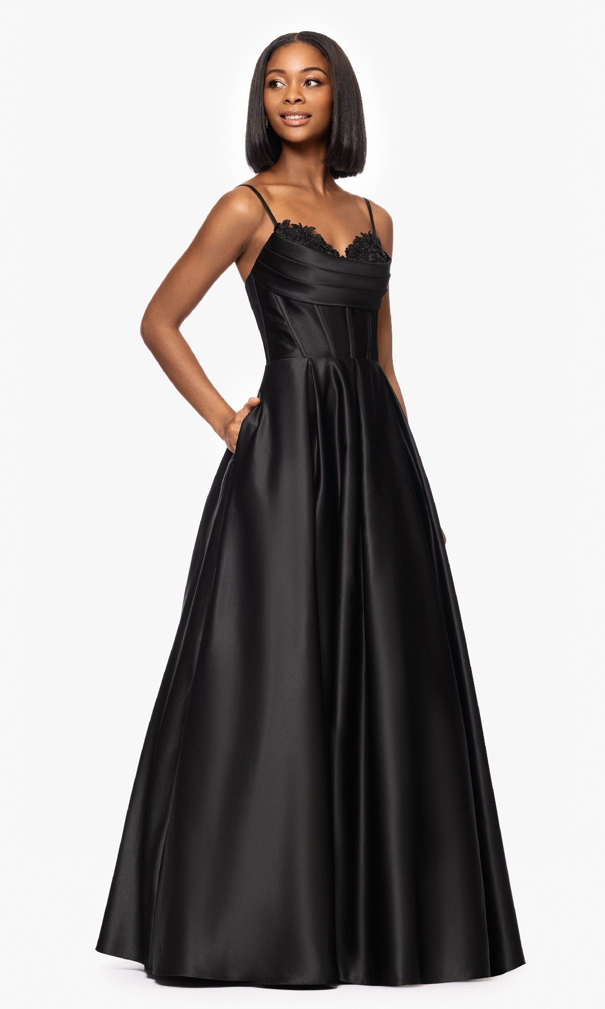 A woman wears the Blondie Nites 5453BN long, sleeveless black satin prom dress with lace appliqué bodice detail, standing against a plain white background.